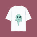 Flat-lay mockup of an oversized white t-shirt featuring a cute, smiling green alien ghost graphic from the anime Dan Da Dan, displayed against a solid mauve background.