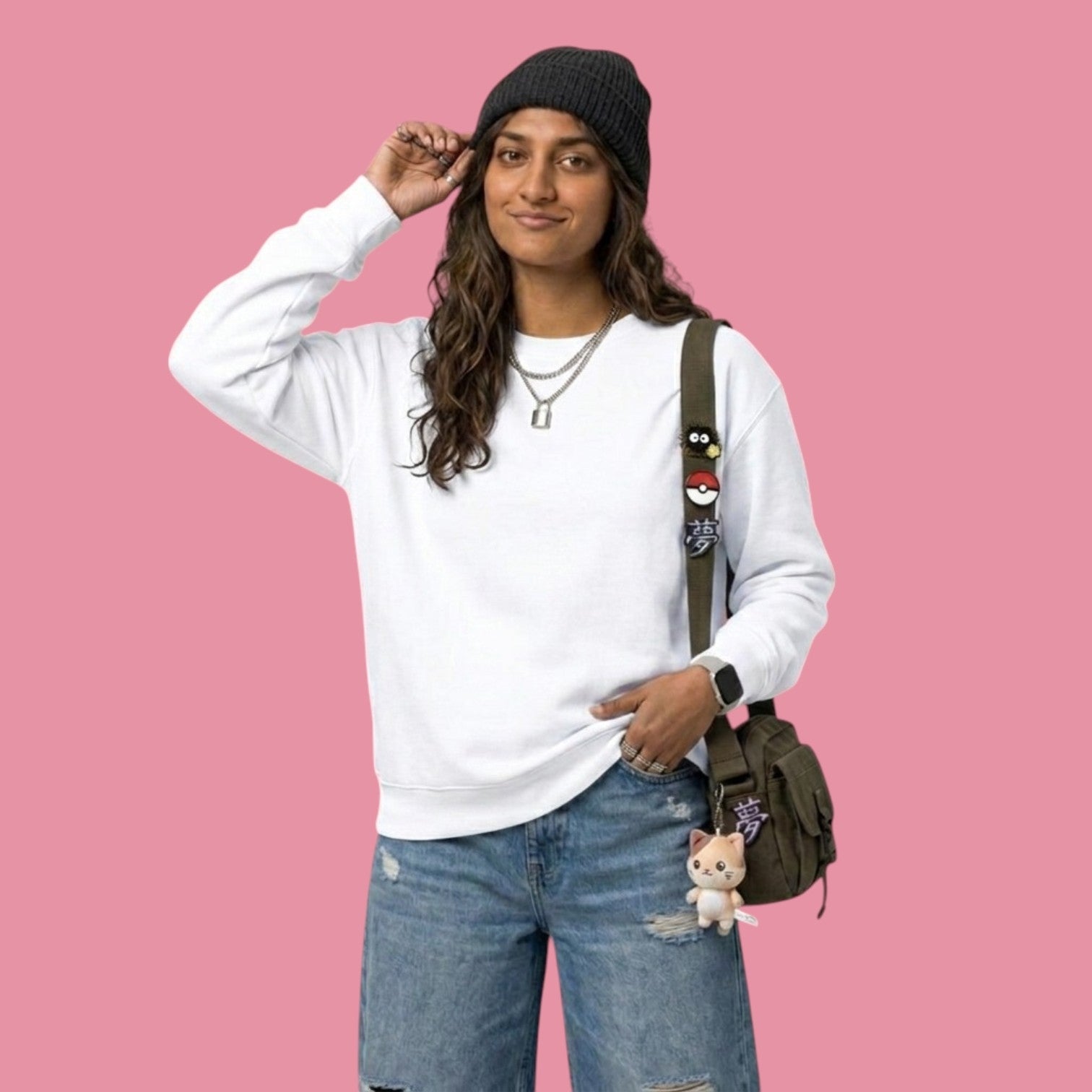 Front view of a model smiling while wearing a classic white crewneck sweatshirt from the Dan da Dan streetwear collection. The model is wearing a black beanie, silver necklaces, baggy blue jeans, and a green messenger bag decorated with anime pins and a cat plushie